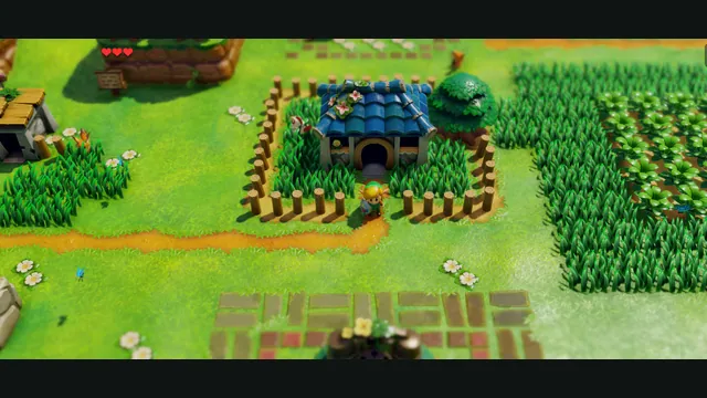 Link outside a blue-roofed house in Mabe Village, with grass, paths and the heart HUD.